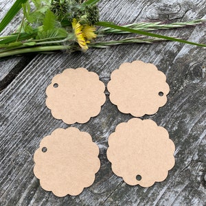 May include: Four brown paper gift tags with scalloped edges and a hole punched in the top. The tags are arranged in a square shape on a wooden surface.