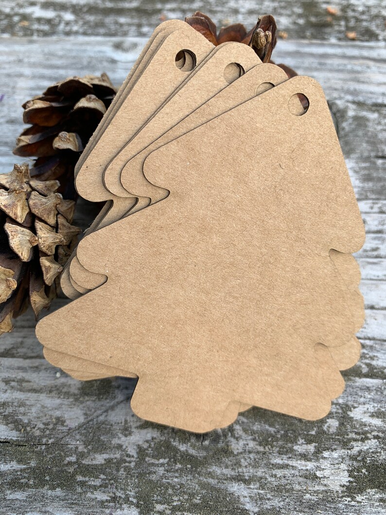 K&ouml;nnte beinhalten: Ein Stapel brauner Papier-Geschenk-Anh&auml;nger in Weihnachtsbaumform mit einem Loch oben.