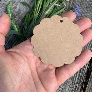 May include: A brown, scalloped, circular gift tag with a hole punched in the top. The tag is held in a person's hand.