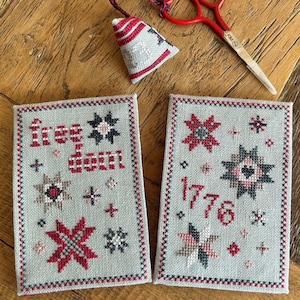 Może przedstawiać: Dwa oprawione haftowane obrazy z motywem w kolorach czerwonym, białym i niebieskim. Pierwszy obraz zawiera napis "Free-dom", a drugi "1776".