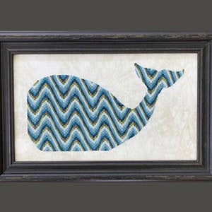 May include: A framed cross-stitch design of a whale with a blue and green chevron pattern.