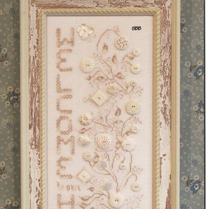 May include: A cross stitch pattern featuring the words "Welcome Home" in a vintage style with a floral design and buttons. The pattern is framed in a distressed white frame and is designed by Karen Kluba.