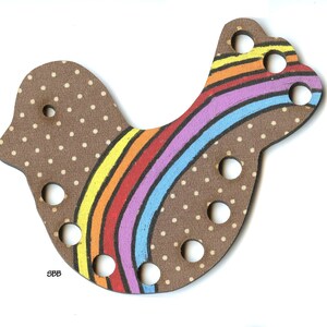 Puede incluir: Juguete de madera con forma de pájaro para atar con un diseño de arcoíris y lunares marrones. El juguete tiene varios agujeros para enhebrar cuerda o hilo.