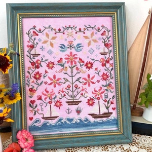 Peut inclure: Un échantillon de point de croix encadré intitulé The Love Boats Sampler présentant un fond en tissu rose avec des motifs floraux brodés, des oiseaux, des ancres et deux petits bateaux naviguant sur des vagues bleues, le tout dans un cadre bleu sarcelle vieilli.