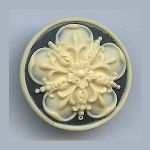 May include: A white ceramic button with a detailed floral design, set against a dark blue background.