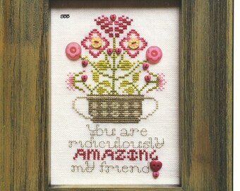 May include: Cross stitch pattern featuring a potted plant with pink flowers and green leaves. The text "You are ridiculously AMAZING my friend" is stitched below the plant.