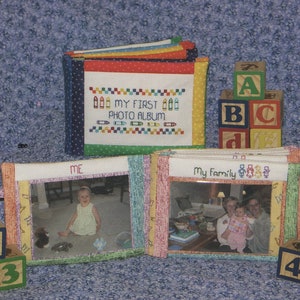 May include: A colorful fabric photo album with a stitched design that says "My First Photo Album". The album is open to reveal two photos, one of a child and one of a family. There are also colorful wooden blocks with letters and numbers.
