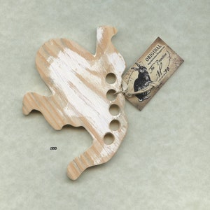 May include: A whitewashed wooden rabbit shaped yarn bowl with five holes for yarn. The bowl has a small tag attached that says "ORIGINAL The Primitive Home".