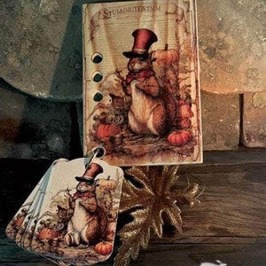 May include: A needlework kit featuring a thankful squirrel with a top hat and autumn leaves. The kit includes six thread drops and the text "Smart Thread Keeps collection THANKFUL SQUIRREL 2024 NEEDLEWORK MARKETPLACE COLLECTION BY THE PRIMITIVE HARE".