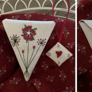 Może przedstawiać: Dwa białe trójkątne ozdoby z tkaniny z czerwonymi i zielonymi haftami. Jedna ozdoba ma wzór czerwonego kwiatu, a druga wzór zielonego liścia. Obie ozdoby mają mały biały guzik.