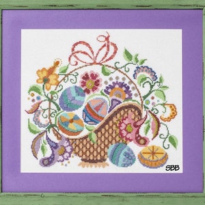 Puede incluir: Un diseño de punto de cruz colorido que presenta una cesta llena de huevos de Pascua, flores y enredaderas. La cesta es marrón con un patrón tejido. Los huevos están decorados con varios patrones y colores. Las flores son rosas, amarillas y moradas. Las enredaderas son verdes y tienen pequeñas hojas. El diseño está enmarcado en un marco de madera verde con un passe-partout morado.