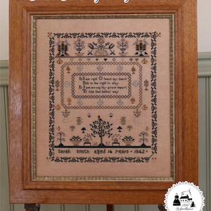May include: A framed antique sampler with a light brown background. The sampler features cross-stitch embroidery with floral and geometric patterns, and text that reads "Sarah Smith, aged 14 years - 1842". The frame is made of wood.