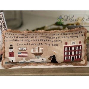 Può includere: Un cuscino beige ricamato a punto croce con un tema nautico. Il cuscino presenta un faro, una nave, una balena, una casa e una donna con un cestino. Il testo sul cuscino recita: "Ho deciso di essere la moglie di un marinaio, di avere una borsa piena di soldi e una vita molto facile! Ma quando lui dice Addio amore mio, parto per il mare."