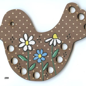 May include: Brown wooden bird-shaped needle minder with white and blue painted flowers. The bird has a polka dot pattern and holes for needles.