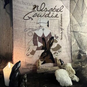 May include: A cross-stitch pattern featuring a vintage illustration of a woman with a rabbit. The text "Isabel Gowdie Witch of Auldearn" is included in the design. The pattern is titled "The Primitive Hare Isabel Gowdie 2024 Needlework Marketplace Collection".