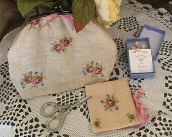 May include: A beige linen coin purse with a pink ribbon and floral embroidery. A matching smaller pouch with a pink ribbon is also pictured. A small blue box with a pink floral charm and a white card with the text "Splendore N. Rocellana Ceramiche" is also pictured.
