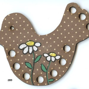 May include: Brown wooden bird shaped sewing thread holder with white daisies and green leaves painted on it. The bird has a polka dot pattern and holes for threading.