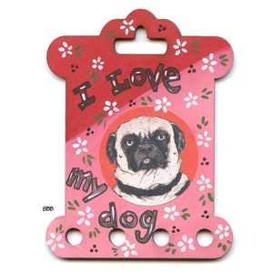Può includere: Un porta-gomitoli in legno rosa e rosso con un'illustrazione di un carlino e il testo "Adoro il mio cane".