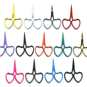 Puede incluir: Un conjunto de 12 tijeras en forma de corazón de varios colores, incluyendo amarillo, blanco, rojo, naranja, verde, dorado, morado, azul, rosa, negro y marrón. Las tijeras están dispuestas en tres filas de cuatro, con los mangos apuntando hacia afuera.