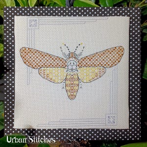 Könnte beinhalten: Kreuzstich-Stickerei eines braunen und gelben Falters mit geometrischen Mustern auf seinen Flügeln. Der Falter ist in einem schwarz-weißen Polka-Dot-Rahmen mit weißem Hintergrund gerahmt.