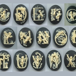 May include: A set of 26 oval-shaped black and white ceramic buttons featuring the letters of the alphabet with cherubs and floral designs.