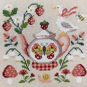 Può includere: Design a punto croce con una teiera con una farfalla, circondata da fragole, fiori, funghi, una lumaca, un'oca e un'ape. Il design utilizza colori rosso, verde, bianco, giallo e rosa su sfondo beige.