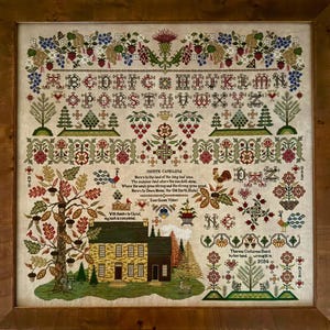 Puede incluir: Un muestrario enmarcado con bordado de punto de cruz sobre tela clara. Incluye un alfabeto, bordes florales, árboles, una casa y el texto North Carolina, 1766, Esse Quam Videri, y Theresa Guitarese Baird by her hand wrought in 2024.
