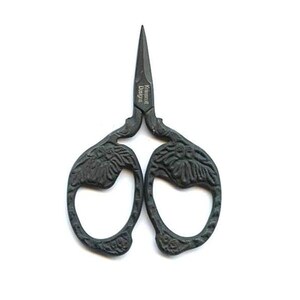 May include: Dark grey, ornate embroidery scissors with a pointed tip. The handles feature a floral design. The text "Kamscott Designs" is printed on the scissors. These scissors are ideal for sewing, embroidery, and crafting projects.