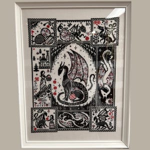 Peut inclure: Une œuvre d'art au point de croix encadrée représentant un dragon central avec des ailes détaillées, entouré de petits panneaux avec des motifs de dragons et de fantaisie. La palette de couleurs est principalement noire, blanche et rouge, créant un contraste saisissant. L'œuvre est encadrée dans un cadre blanc.