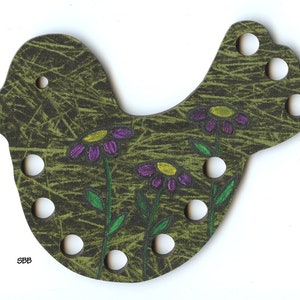 May include: A bird-shaped wooden craft with a green and brown textured background, featuring purple flowers with yellow centers. The bird has several white holes and the initials "SBB" are visible.