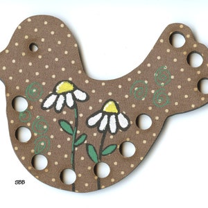 May include: A brown wooden bird-shaped craft with white polka dots and painted daisies. The bird has several holes and green swirls. The letters "SBB" are in the lower left corner. A decorative item for crafts.