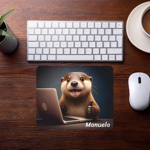 Könnte beinhalten: Ein rechteckiges Mauspad mit einem braunen Otter, der vor einem silbernen Laptop sitzt und den Daumen hochhält. Der Name Manuela ist in weißer Schrift unten rechts auf dem Mauspad aufgedruckt, das auf einem dunklen Holztisch liegt.