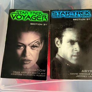May include: Two Star Trek paperback books. The left book is Star Trek Voyager Section 31 Shadow by Dean Wesley Smith and Kristine Kathryn Rusch. The right book is Star Trek Deep Space Nine Section 31 Abyss by David Weddle and Jeffrey Lang.