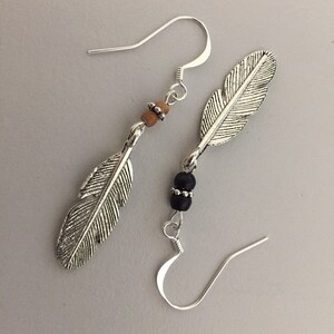 May include: Silver feather earrings with black and brown beads. The earrings have a simple hook fastening.