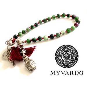 May include: A green and red gemstone bracelet with silver charms, including a small Buddha charm and a tassel. The bracelet is on a white background with the text "MY VARDO" below it.