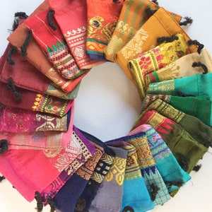 May include: A collection of colourful fabric drawstring pouches arranged in a circle. The pouches are made of various fabrics with intricate patterns and designs. The pouches are all different sizes and shapes.
