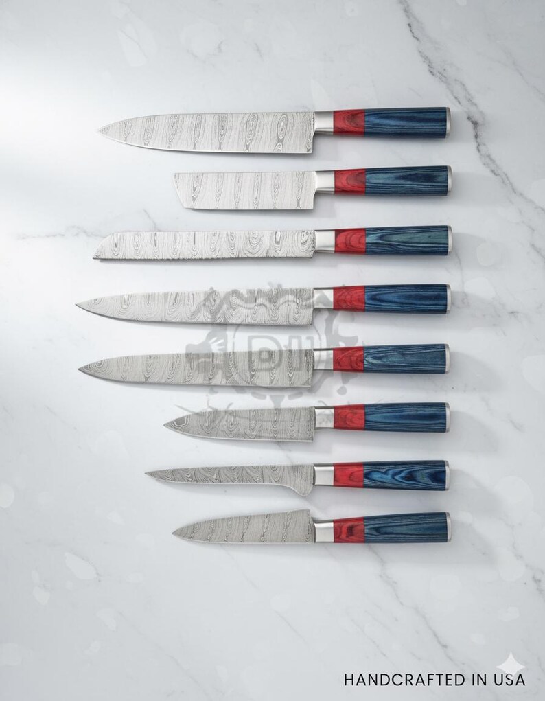 Puede incluir: Un juego de siete cuchillos de cocina de acero inoxidable con hojas estampadas y mangos rojos, plateados y azules. Los cuchillos est&aacute;n colocados sobre una superficie de m&aacute;rmol blanco. El texto "HANDCRAFTED IN USA" est&aacute; en la parte inferior.