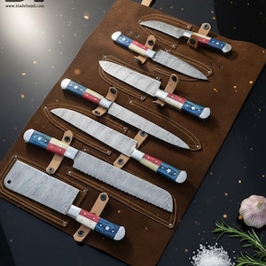 Può includere: Un set di sette coltelli in acciaio Damasco con manici con design a stelle e strisce rosse, bianche e blu, esposti in un rotolo di coltelli in pelle marrone. Le lame hanno un aspetto unico.