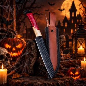 May include: A fixed-blade knife with a black hammered metal finish and a handle featuring a red and light wood pattern. The knife is accompanied by a brown leather sheath with a metal rivet, positioned upright on a dark wooden surface.