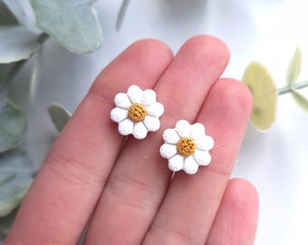 May include: A pair of white daisy earrings with yellow centers. The earrings are small and delicate, perfect for adding a touch of whimsy to any outfit.