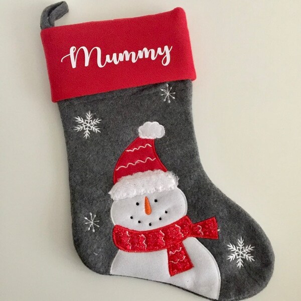 May include: A gray Christmas stocking with a red cuff and a snowman applique. The cuff is embroidered with the word "Mummy".