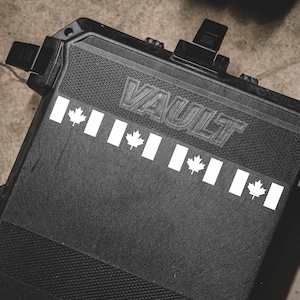 May include: Black rectangular storage container with the word "VAULT" embossed on the top. The container has a textured surface and is decorated with white Canadian flag graphics.