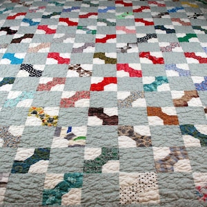 May include: A patchwork quilt with a blue background and a pattern of white squares with colorful bow tie shapes in each square.