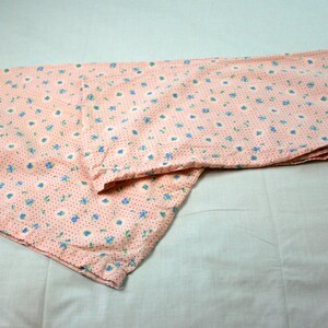 May include: A pink fabric with a small floral pattern in blue and white. The fabric is folded in half and the edges are visible.