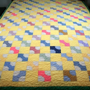 May include: A handmade quilt with a yellow background and a repeating pattern of colorful squares. The squares are filled with various patterns and colors, including blue, pink, and green. The quilt has a green border.