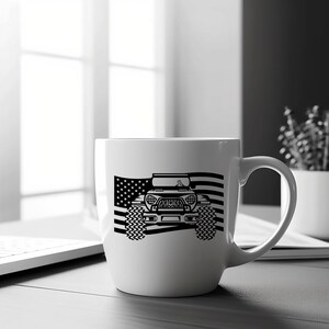 May include: White ceramic mug featuring a black and white image of a Jeep driving over an American flag.