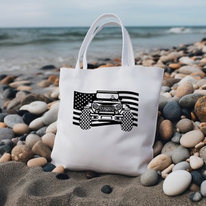 May include: White canvas tote bag featuring a black and white graphic of a Jeep against an American flag background. The Jeep has a black grille and black tyres.