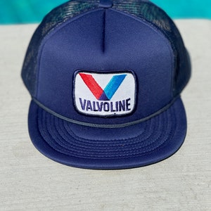 May include: A navy blue trucker hat with a mesh back and a white patch with a red and blue logo that says "Valvoline".