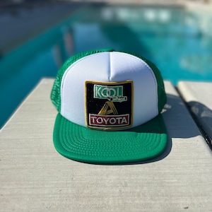 May include: A green and white trucker hat with a black and gold patch that says "KOOL" and "TOYOTA" with a green car on the patch.