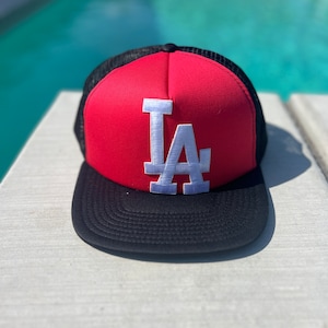 May include: A red and black baseball cap with a white "LA" logo embroidered on the front.